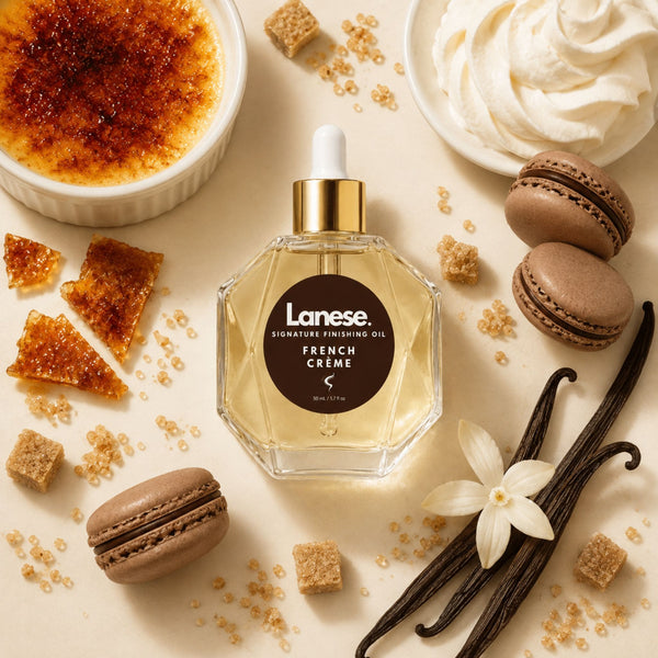 A bottle of Lanese French Crème finishing oil is centered in a styled flat-lay with whipped cream, macarons, brown sugar cubes, vanilla beans, and a flower on a warm cream background.