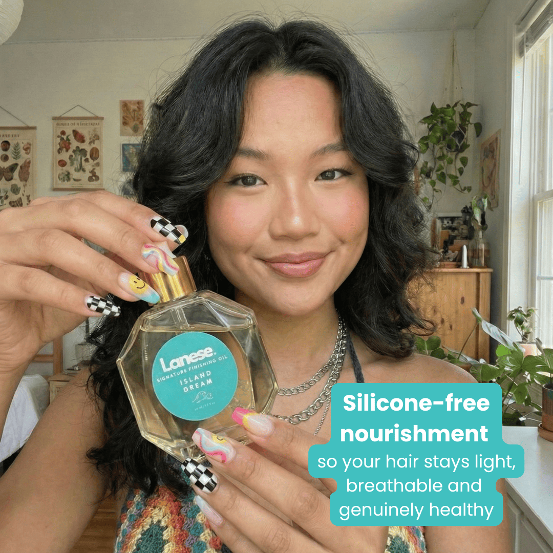 A smiling woman with wavy dark hair holds the Island Dream oil bottle. She has a trendy checkered and swirl manicure. A teal text box at the bottom right reads: "Silicone-free nourishment so your hair stays light, breathable and genuinely healthy."