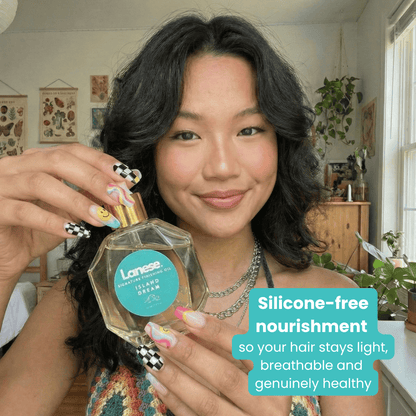 A smiling woman with wavy dark hair holds the Island Dream oil bottle. She has a trendy checkered and swirl manicure. A teal text box at the bottom right reads: "Silicone-free nourishment so your hair stays light, breathable and genuinely healthy."