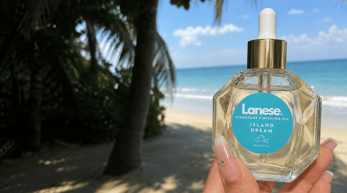 A hand holds a bottle of Lanese Island Dream Finishing Oil in front of a tropical beach background with palm trees and ocean water.